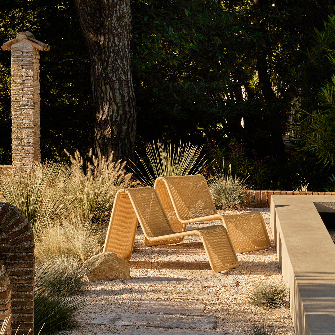 Beige modern lounge chair with a sleek, minimalist design, set against natural greenery and earthy tones.