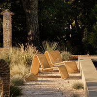 Beige modern lounge chair with a sleek, minimalist design, set against natural greenery and earthy tones.