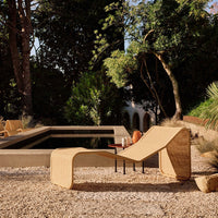 Lounge chair featuring a natural beige hue and smooth, curved lines, set against a lush green garden backdrop.