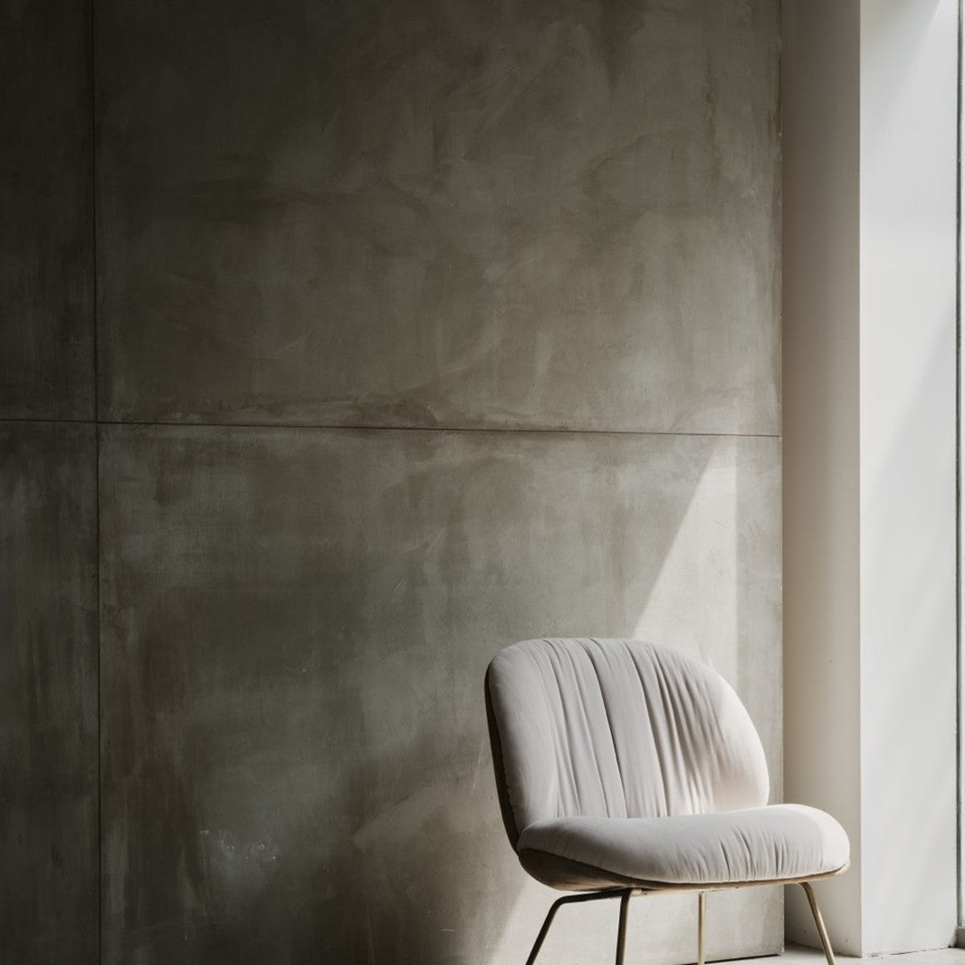 Beige upholstered chair against a textured gray wall, featuring soft lines and minimalistic design.