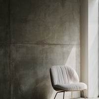 Beige upholstered chair against a textured gray wall, featuring soft lines and minimalistic design.