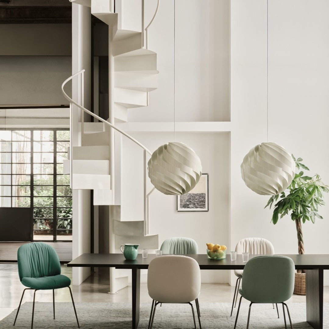 "Modern dining area with mint green and soft peach chairs, white spiral lamps, and neutral wall tones."