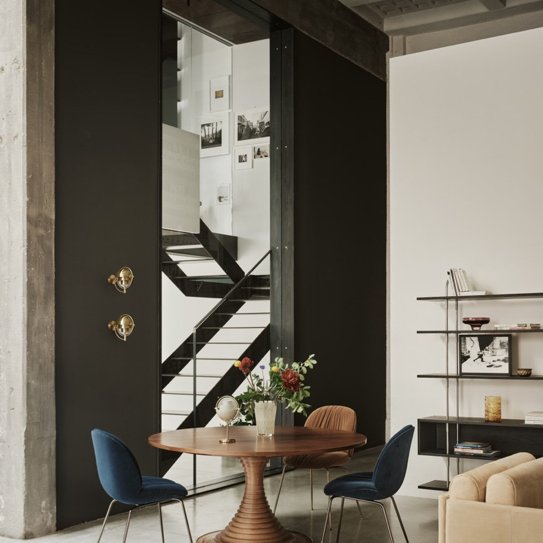 Modern interior with black and white walls, gold accents, blue and tan chairs, and a wooden table featuring floral decor.