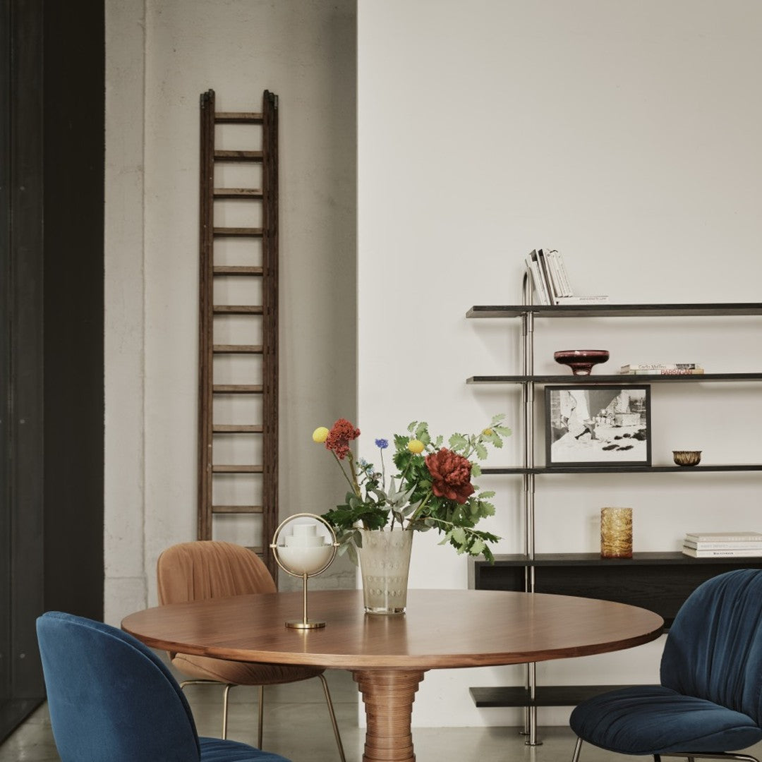 "Round wooden table with deep blue and rust chairs, featuring colorful floral arrangement and modern shelving unit."