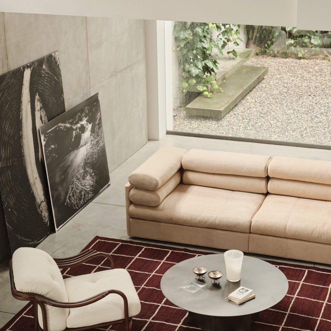 Beige sectional sofa with grid pattern, red and white geometric rug, gray circular table in a modern, minimalist living space.