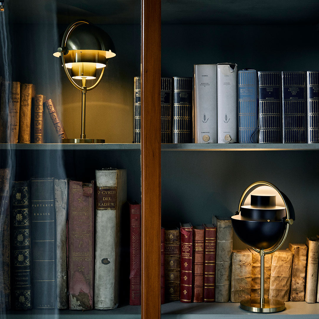 "Gold and black table lamps beside vintage books in hues of burgundy and navy on a dark shelf backdrop."
