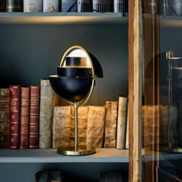Black two-toned lamp with a gold base, positioned among vintage books on a dark shelf. Elegant and modern design.