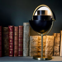 Black and gold modern lamp with circular shapes, contrasting with vintage red and brown books on a dark background.