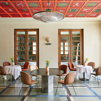 Elegant dining room featuring red patterned ceiling, neutral walls, and stylish brown and beige chairs with white tables.
