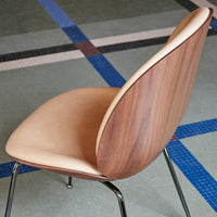 Mid-century modern chair featuring a warm walnut wood finish and smooth tan leather upholstery against a geometric floor pattern.