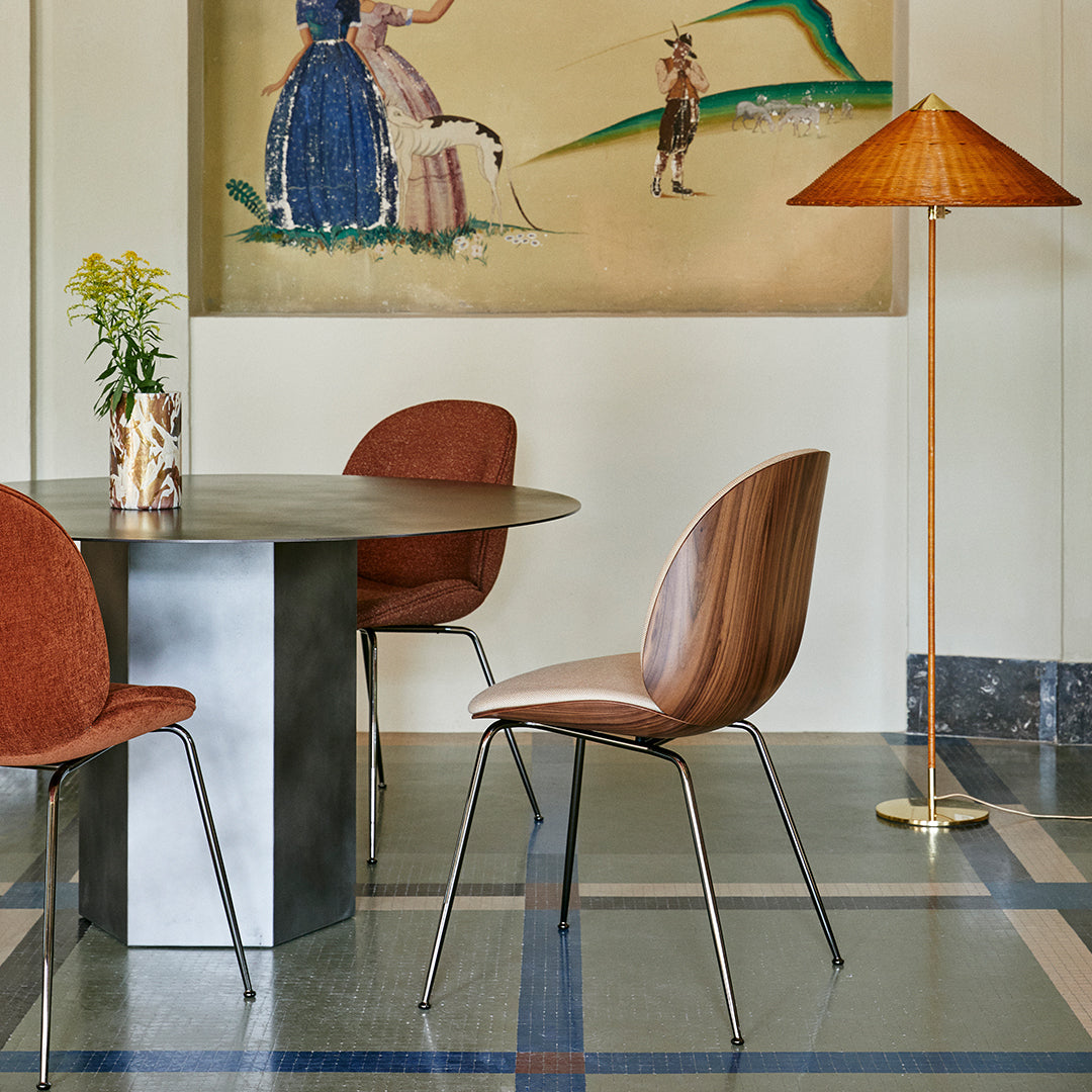 "Round gray table with brown upholstered chairs, golden lamp, and artwork featuring soft colors and floral patterns."