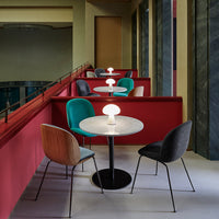 Colorful dining area with teal, gray, and wood-patterned chairs against red booths and marble tables. Modern design elements.