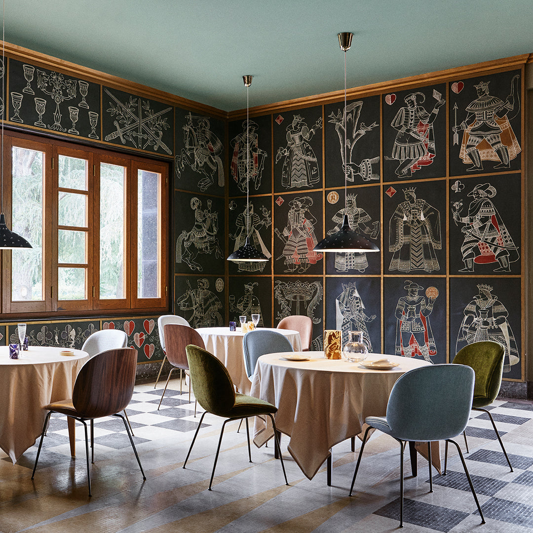 "Elegant dining area featuring patterned dark wall art, soft beige tables, and colorful chairs in muted shades."