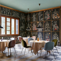 "Elegant dining area featuring patterned dark wall art, soft beige tables, and colorful chairs in muted shades."