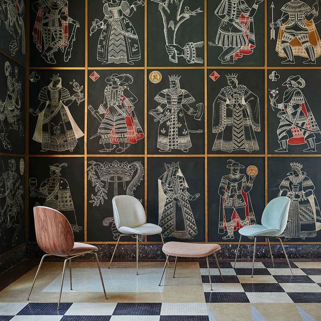 Four stylish chairs in pastel colors against a dark patterned wall featuring intricate illustrations.