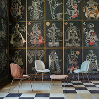Four stylish chairs in pastel colors against a dark patterned wall featuring intricate illustrations.