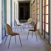 Four minimalist chairs with soft beige upholstery and black metal legs arranged in a spacious hallway with natural light.