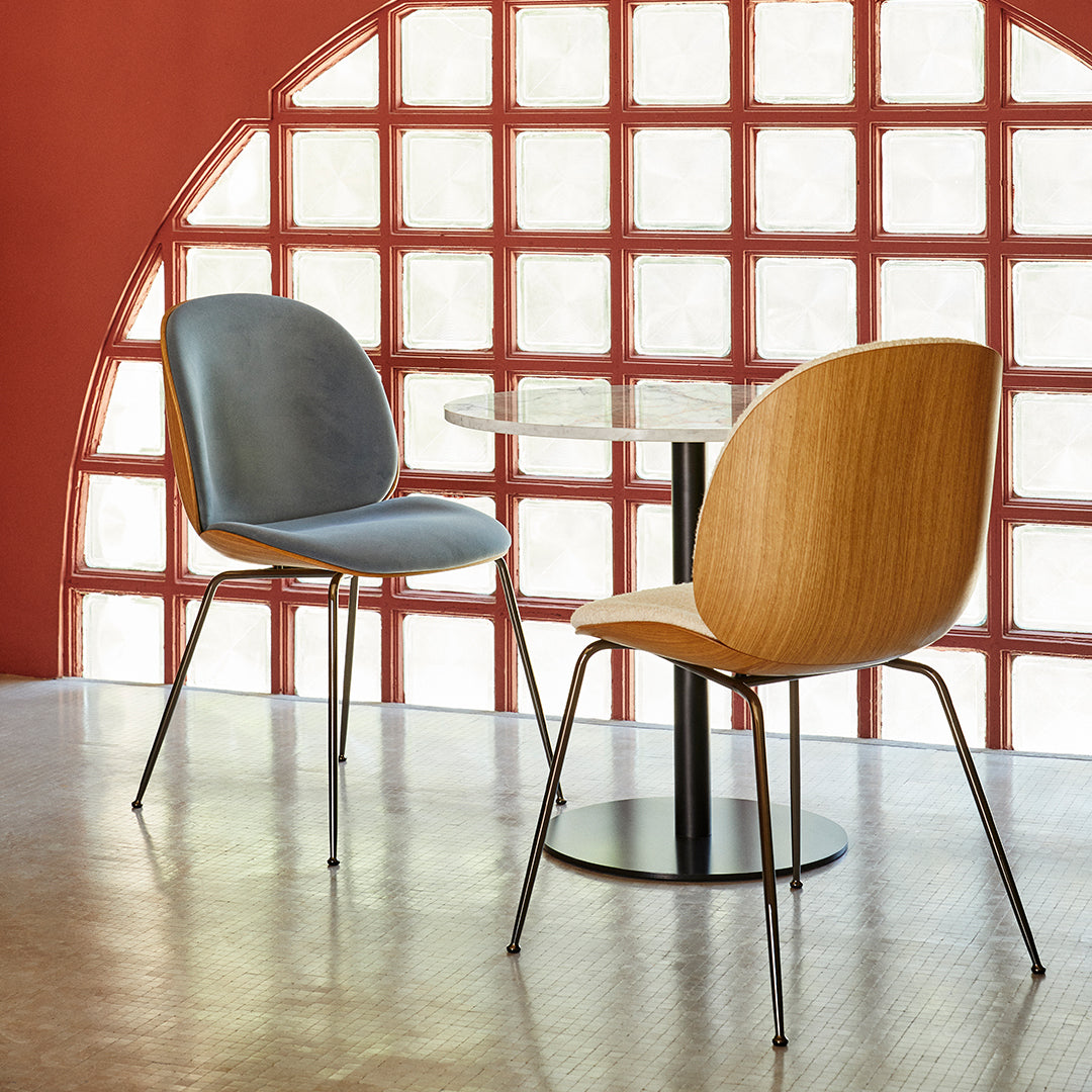 Modern chairs with blue upholstery and wooden backs, set against a red wall with a patterned glass backdrop.