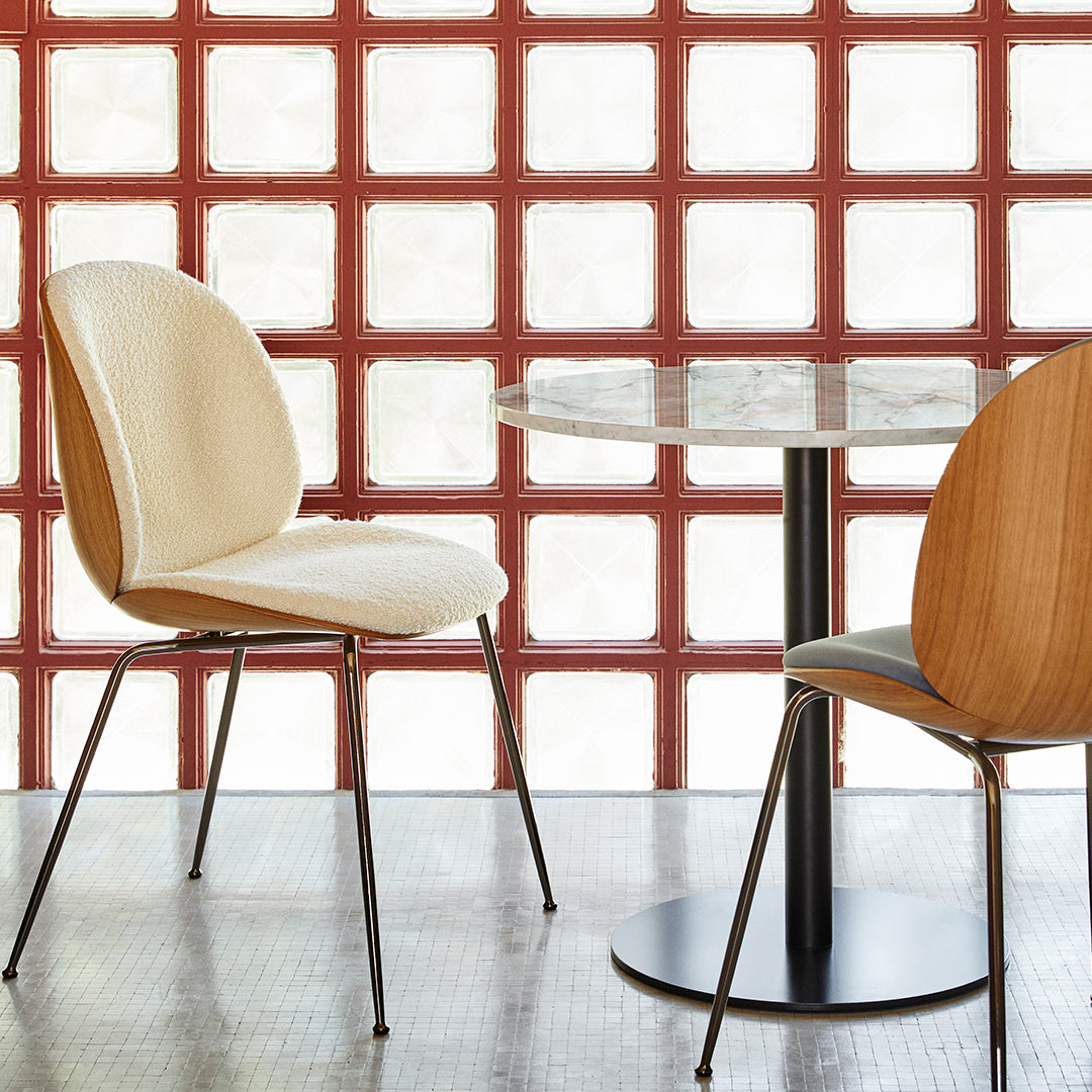 Elegant cream and wood dining chairs with a sleek black table set against a textured red glass block wall.
