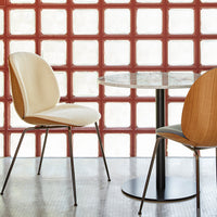 Elegant cream and wood dining chairs with a sleek black table set against a textured red glass block wall.