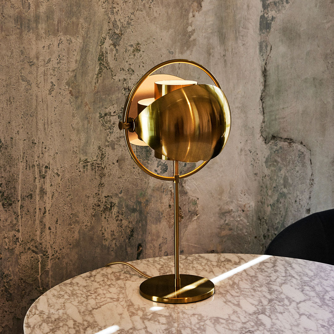 Gold modern table lamp with sleek lines and a round shape, set against a textured concrete background.