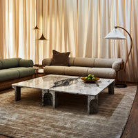 Modern coffee table with gray marble top, featuring unique veining, set against warm beige curtains and earthy tones.