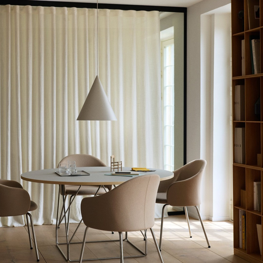 Modern beige chairs around a white table, with soft cream curtains and a sleek gray pendant light overhead.
