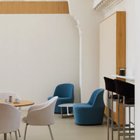 Modern lounge area featuring teal and beige chairs with light wood accents and a neutral wall backdrop.