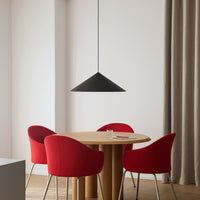 Modern black pendant light over a round wooden table with bold red chairs, set against a neutral backdrop.