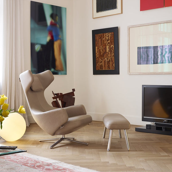 Beige modern chair with a matching ottoman, featuring soft curves and sleek metal legs, set against colorful wall art.