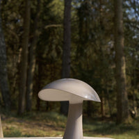 Minimalist beige mushroom-shaped lamp with a smooth, glossy finish, set against a natural forest backdrop.