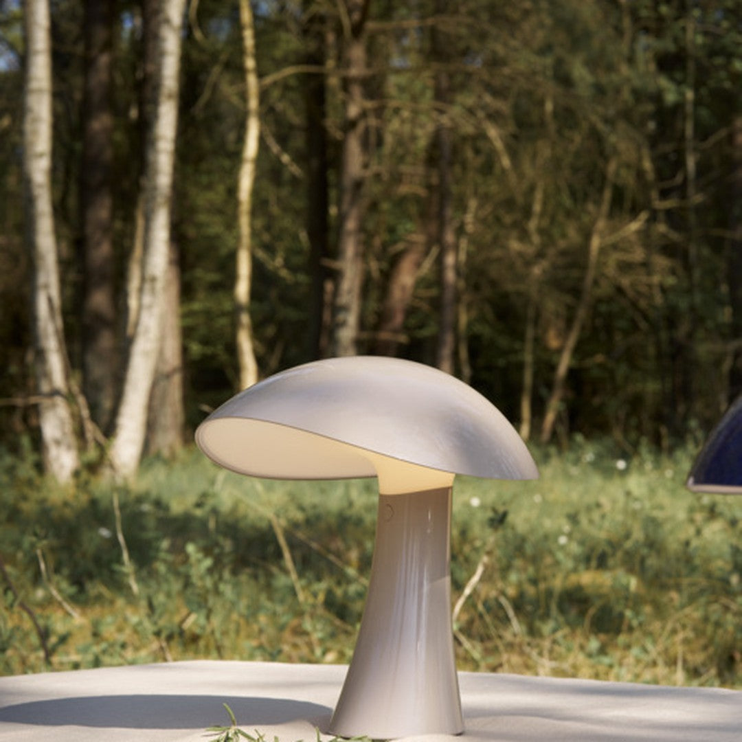Mushroom-shaped lamp in soft gray with a smooth, glossy finish, set against a natural outdoor backdrop.