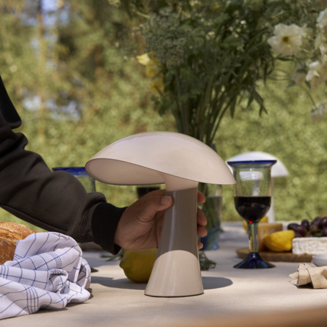 Beige mushroom-shaped table lamp with a smooth finish, set against a natural outdoor backdrop.