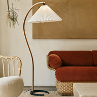 "Minimalist floor lamp with a white pleated shade, complemented by a warm brown and terracotta-colored sofa."