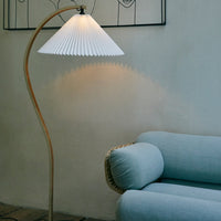 Elegant white pleated lampshade with a smooth wooden base, illuminating soft pastel blue sofa beneath.