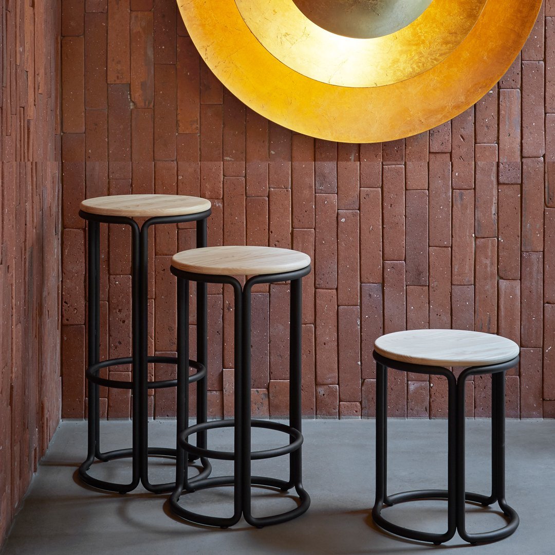 Set of three modern bar stools with black metal frames and round cream seats against a rustic brick wall.
