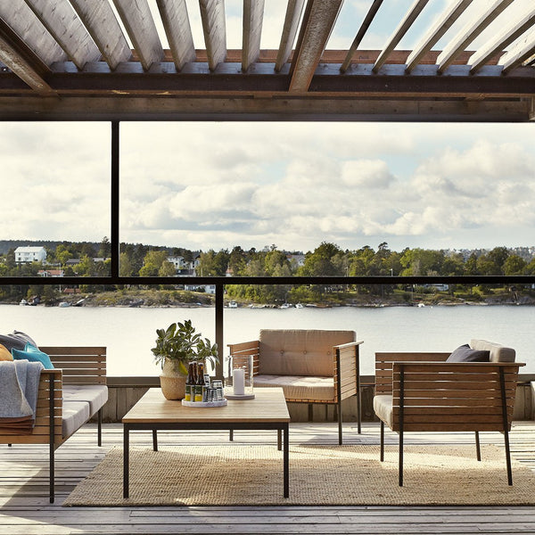 "Stylish outdoor seating in muted earth tones, complemented by a natural wood table and scenic waterfront backdrop."