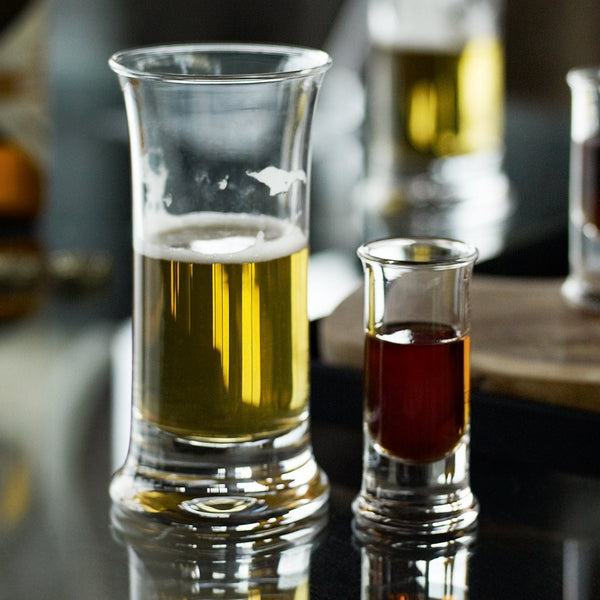 "Clear glass shot and beer glasses showcasing golden and deep amber liquids reflecting light."