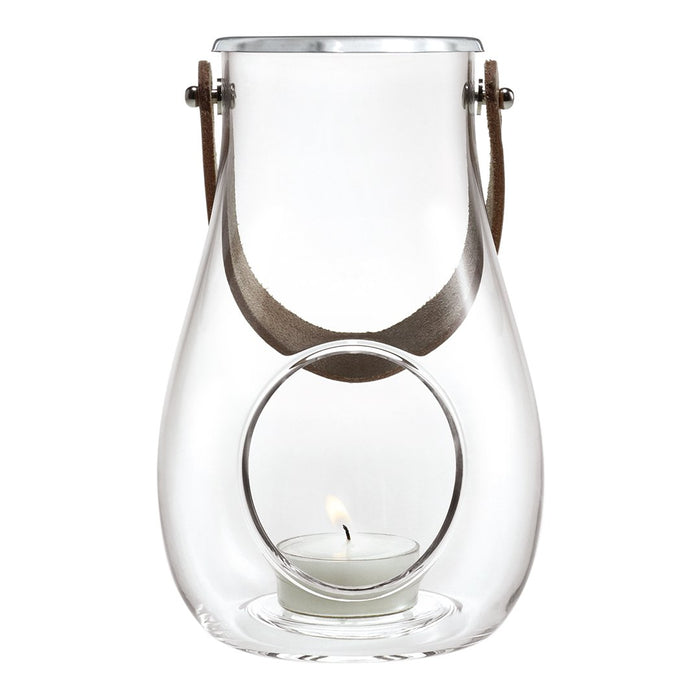Clear glass lantern with a circular cutout, accented by a brown leather handle and a subtle candle glow.