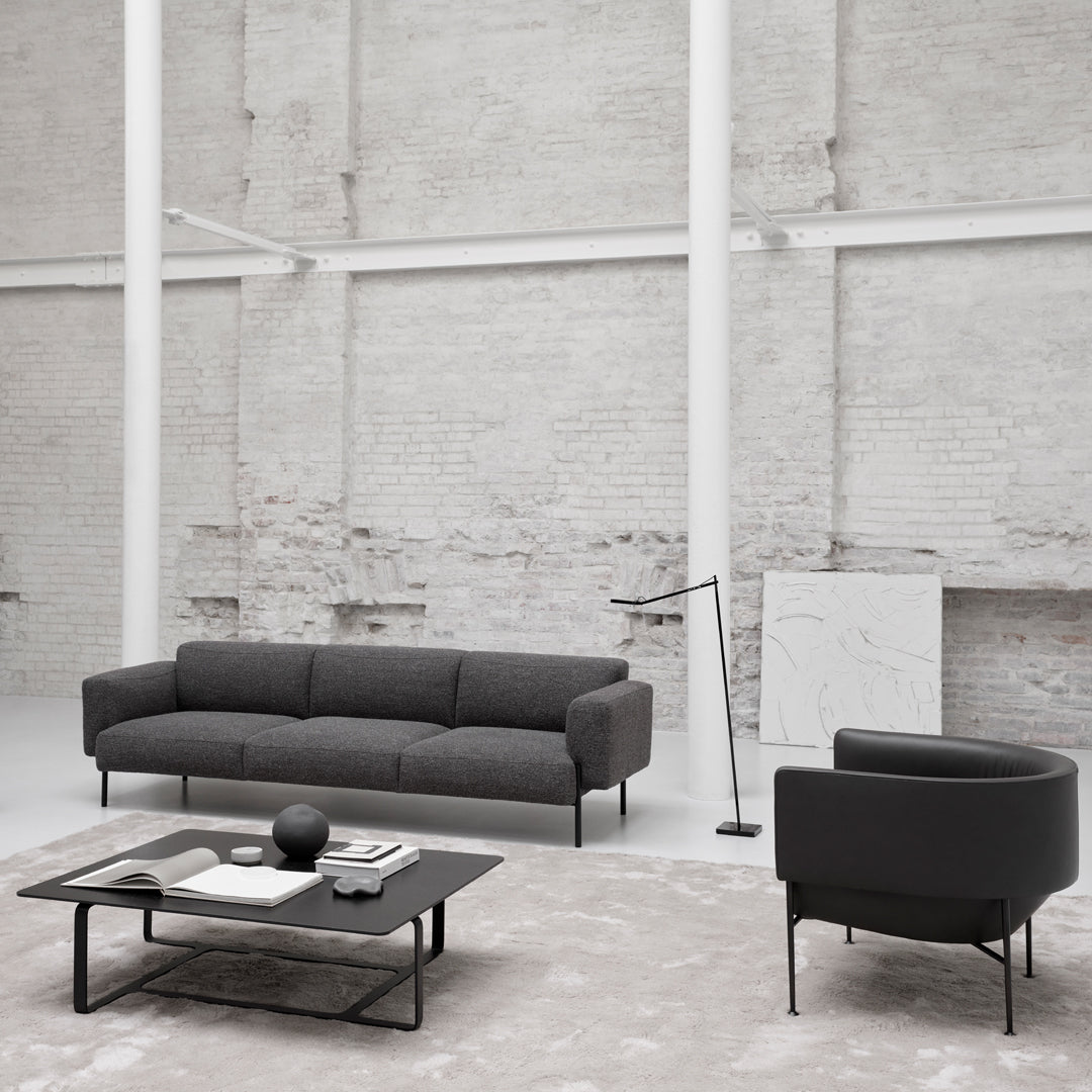 "Modern black sofa and round chair against a minimalist light-gray background with soft textures."