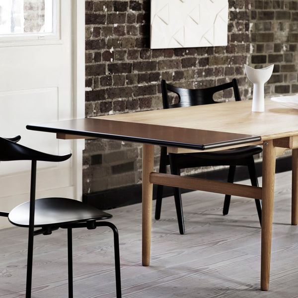 Wooden table with black tabletop, featuring a natural wood finish and minimalistic design, set against a textured brick wall.