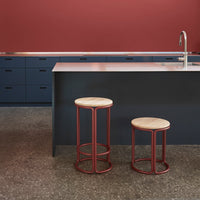 "Red metal stools with natural wood seats against a dark blue kitchen backdrop and warm red wall."