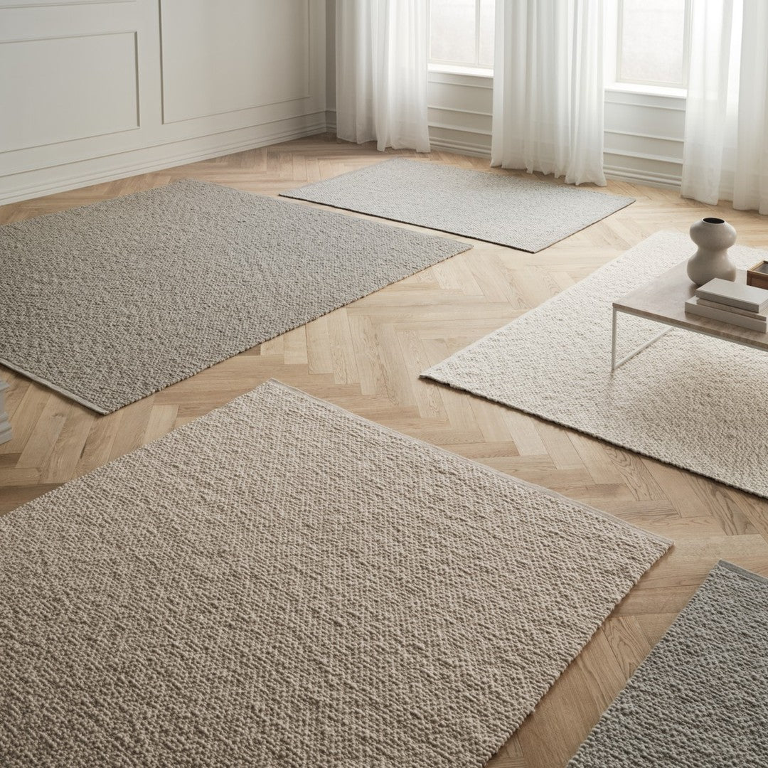 Neutral-toned area rugs in varying textures and patterns on a light wood floor, featuring soft beige and gray shades.