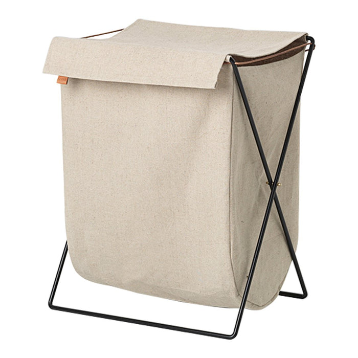 Beige fabric laundry basket with a black metal frame and a brown leather strap accent. Minimalist design.