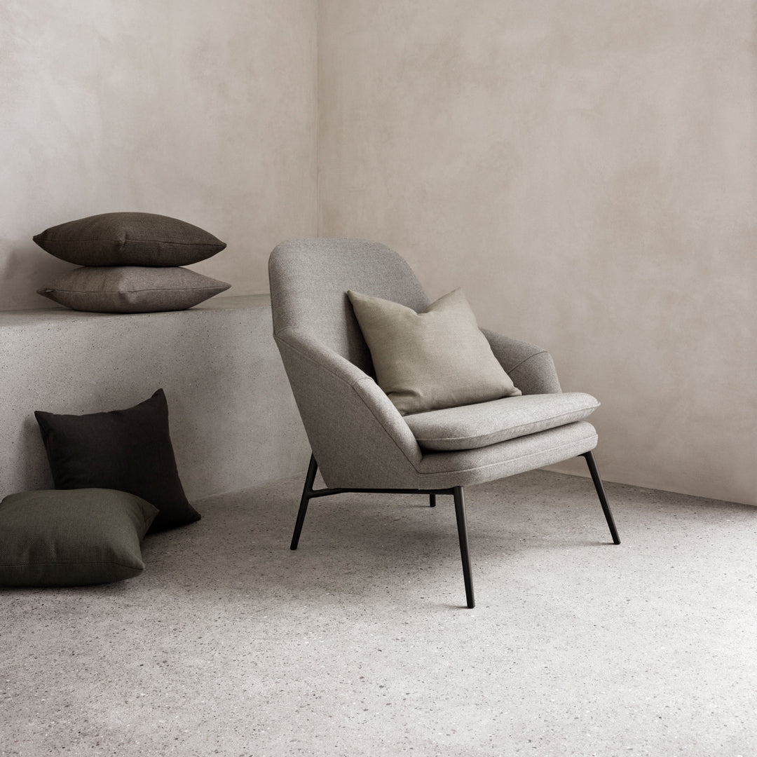 Gray armchair with textured fabric, accented by dark green and brown cushions against a neutral backdrop.