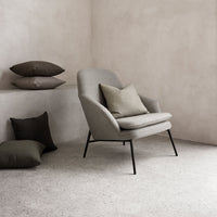 Gray armchair with textured fabric, accented by dark green and brown cushions against a neutral backdrop.