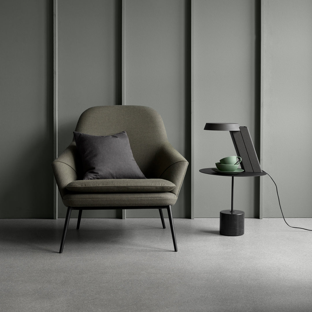 Sleek olive green chair with a dark gray pillow, paired with a minimalist black side table against a muted gray backdrop.