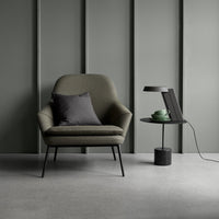 Sleek olive green chair with a dark gray pillow, paired with a minimalist black side table against a muted gray backdrop.