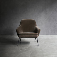 Brown velvet accent chair with smooth, modern lines and sleek black legs, set against a minimalist gray backdrop.