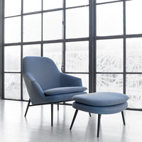 Blue upholstered armchair and ottoman with sleek black legs, set against a light-filled window backdrop.